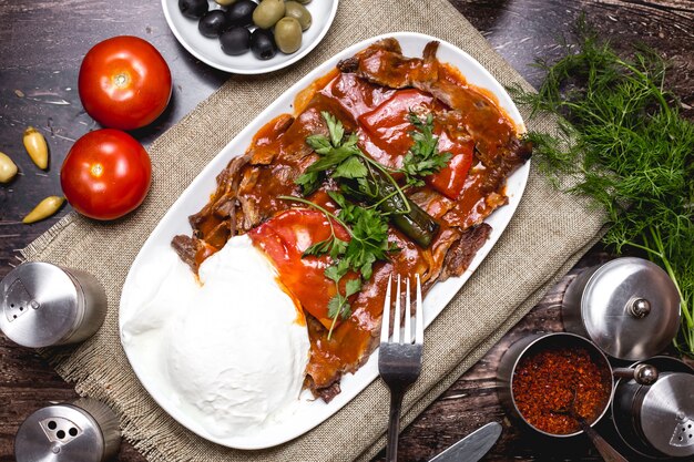 Vista superior del kebab iskender adornado con tomate y perejil servido con yogurt