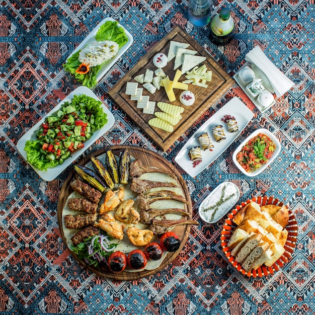 Vista superior de kebab mixto servido con ensalada de verduras frescas plato de queso y rollos de berenjena en una alfombra colorida