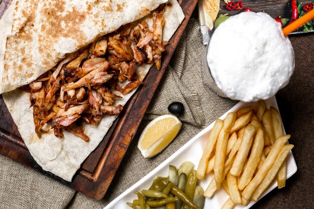 Vista superior de kebab de pollo con pan plano servido con papas fritas encurtidos limón y ayran