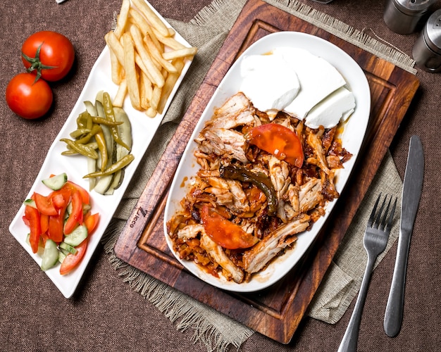 Vista superior de kebab de pollo con salsa de tomate servido con yogur, papas fritas encurtidos y verduras