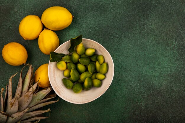 Vista superior de kinkans en un recipiente con limones aislado sobre una superficie verde con espacio de copia