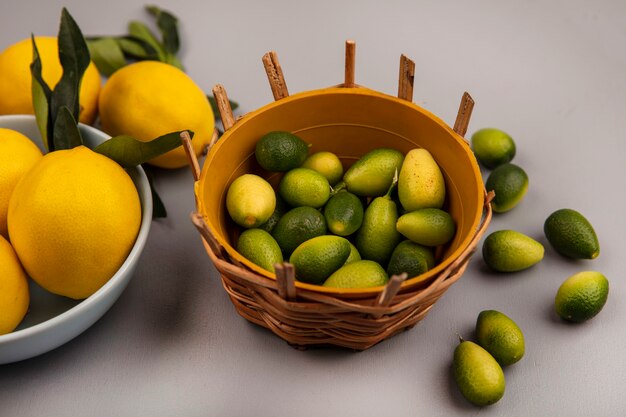 Vista superior de kinkans verdes frescas en un balde con limones en un recipiente con kinkans aislado sobre un fondo blanco.