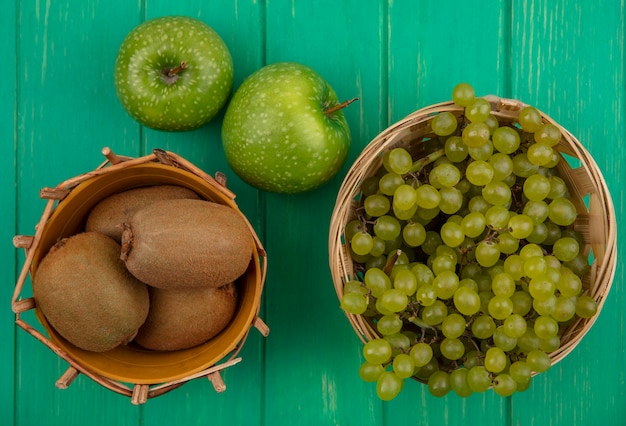 Vista superior de kiwi con uvas verdes en cestas y manzanas verdes sobre un fondo verde