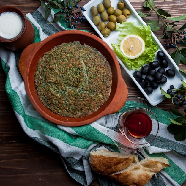 Vista superior kuku con vaso de té y una variedad de aceitunas y pan en plato de arcilla