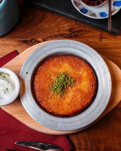 Vista superior de kunefe tradicional postre turco con pistacho en polvo sobre una mesa de madera