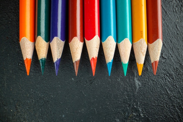 Vista superior de lápices de colores forrados sobre fondo oscuro