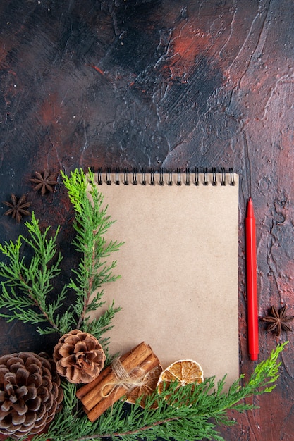 Vista superior lápiz rojo un cuaderno ramas de pino anís estrellado rodajas de limón secas en la superficie de color rojo oscuro espacio de copia