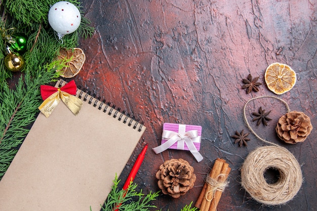 Vista superior lápiz rojo un cuaderno ramas de pino árbol de navidad juguetes de bolas hilo de paja anís estrellado en la superficie de color rojo oscuro espacio de copia