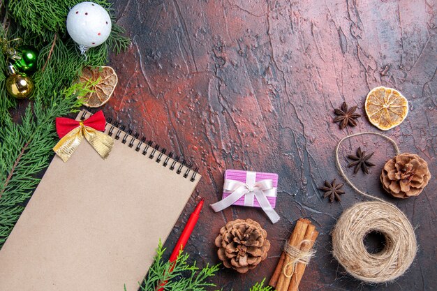 Vista superior lápiz rojo un cuaderno ramas de pino árbol de navidad juguetes de bolas hilo de paja anís estrellado en la superficie de color rojo oscuro espacio de copia