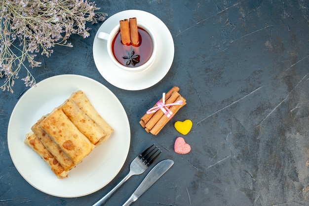 Vista superior de lavash envuelve en un plato y cubiertos, una taza de té negro canela limones sobre fondo negro