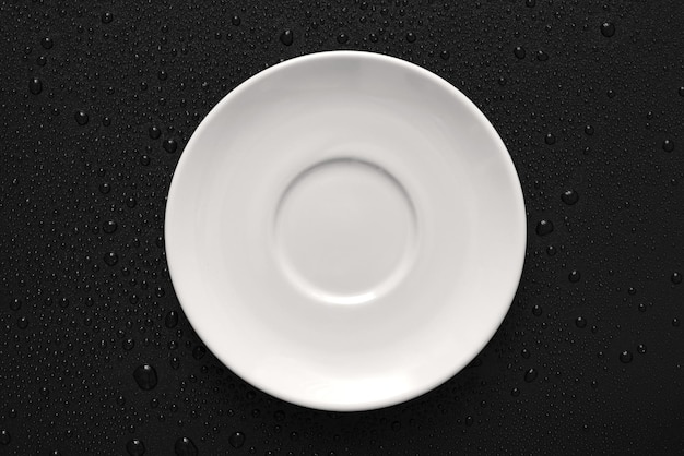 Vista superior Lay Flat de plato blanco sobre fondo negro húmedo con textura áspera