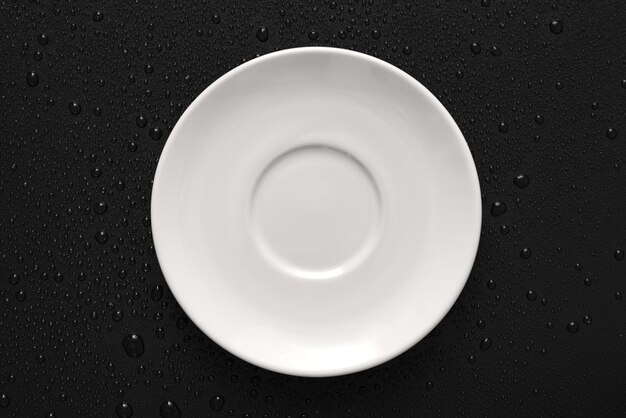 Vista superior Lay Flat de plato blanco sobre fondo negro húmedo con textura áspera