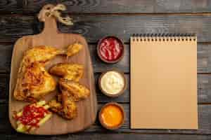 Foto gratuita vista superior desde lejos cuaderno de crema de pollo apetitosas papas fritas pollo y salsa de tomate en la tabla de cortar de madera junto a cuencos de salsas de colores en la mesa oscura