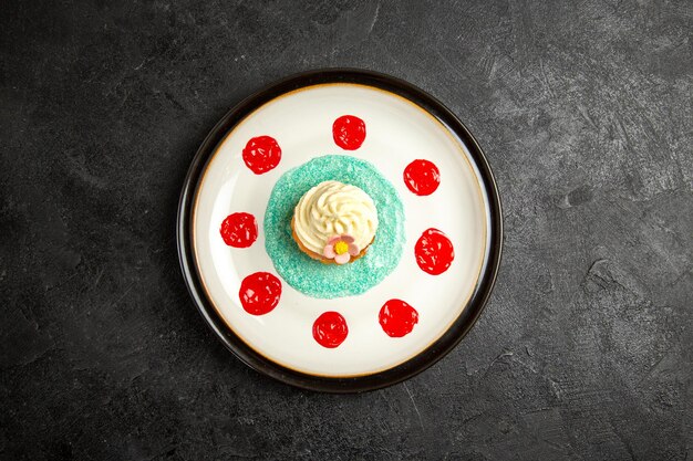 Vista superior desde lejos cupcake en el plato cupcake con salsa en el plato blanco en el centro de la mesa oscura