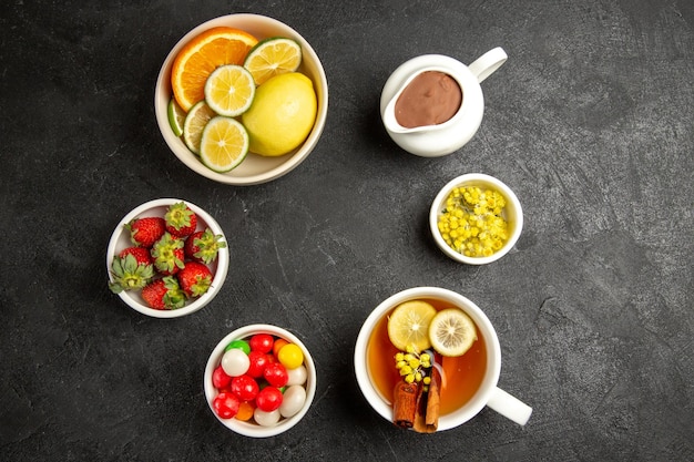 Vista superior desde lejos dulces en la mesa cuencos de hierbas y fresas junto a la taza de té de hierbas con palitos de canela y limón