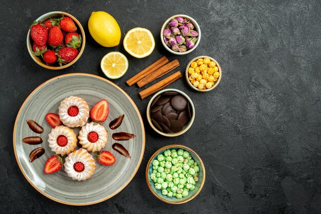 Vista superior desde lejos dulces con té apetitosas galletas con té negro de fresa con limón hizelnuts tazones de chocolate y diferentes dulces en el lado izquierdo de la mesa