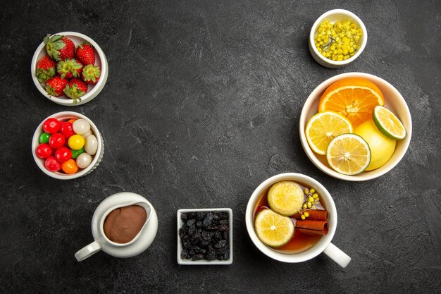 Vista superior desde lejos dulces con té, una taza de té de hierbas con canela, tazones de fuente de dulces, crema de chocolate, fresas y frutas cítricas en la mesa