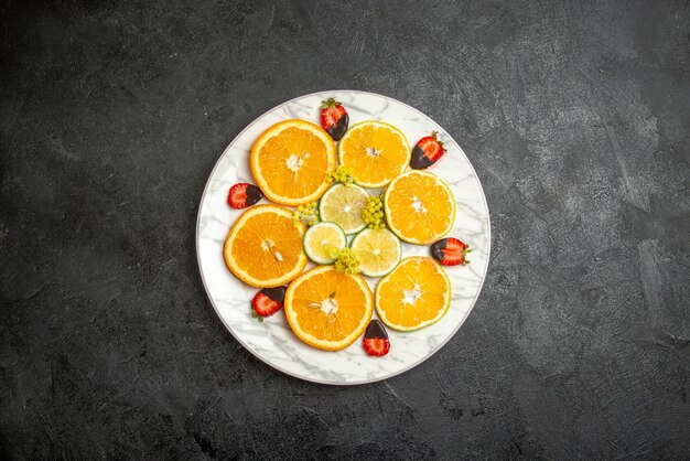 Vista superior desde lejos frutas en un plato en rodajas de naranja limón y fresas cubiertas de chocolate en un plato blanco en el centro de la mesa