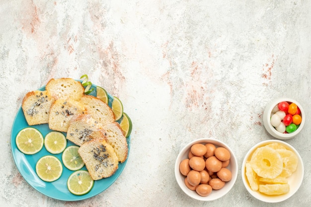 Vista superior desde lejos pan de limón pan blanco con hierbas limón en el plato junto a cuencos de caramelos sobre la mesa