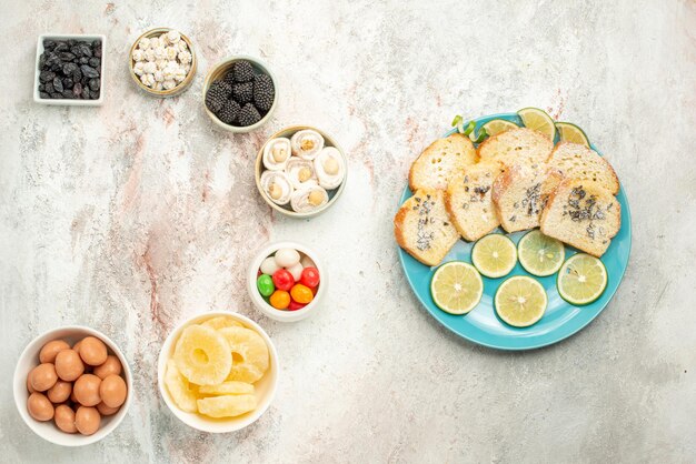 Foto gratuita vista superior desde lejos pastel de limón siete tazones de dulces a la izquierda y plato de trozos de pastel con limón en el lado derecho de la mesa