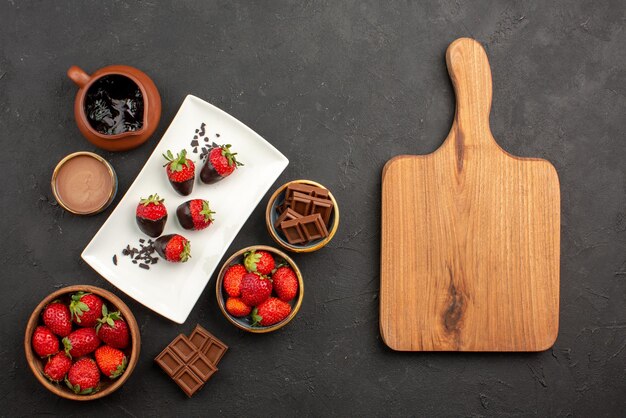 Vista superior desde lejos tablero de cocina de fresas de chocolate con crema de chocolate y fresas fresas cubiertas de chocolate chocolate junto a la tabla de cortar de madera