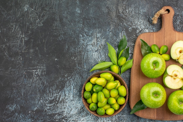 Vista superior desde lejos tazón de frutas de frutas cítricas manzanas con hojas en la tabla de cortar