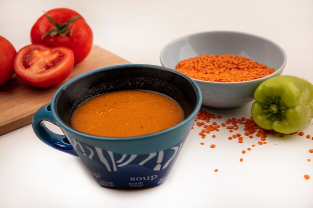 Vista superior de lentejas naranjas frescas en un tazón con sopa de lentejas naranja en un tazón con tomates en una tabla de cocina de madera sobre una pared blanca