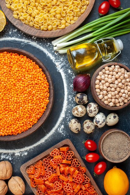 Vista superior de lentejas naranjas con huevos, nueces, verduras, pasta cruda y condimentos sobre fondo oscuro, dieta cruda, cocina, foto en color, pastel