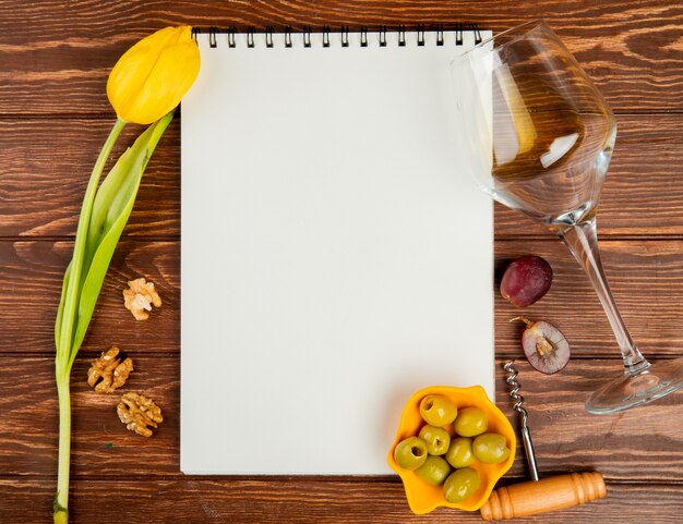 Vista superior de la libreta con sacacorchos de uva vino blanco oliva nuez y flor sobre fondo de madera con espacio de copia