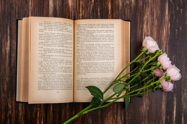 Vista superior del libro abierto con rosas rosadas sobre una superficie de madera