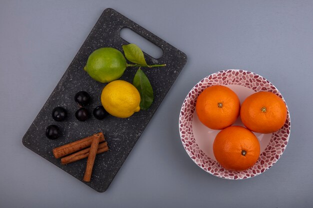 Vista superior de lima con limón, cereza, ciruela y canela sobre una tabla de cortar con naranjas en un plato sobre un fondo gris