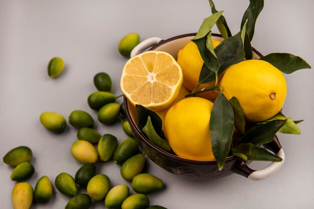 Vista superior de limones amarillos frescos con hojas en un recipiente con kinkans aislado en una pared blanca