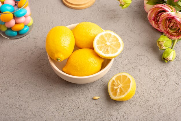 Una vista superior limones frescos agrios maduros enteros con coloridos caramelos flores secas cítricos suaves vitamina amarilla amarilla en el escritorio de crema
