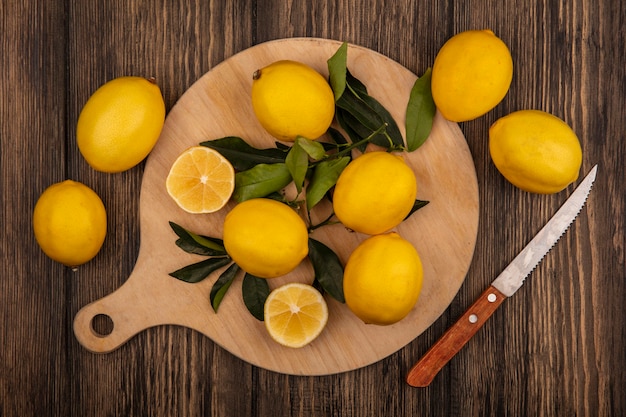 Vista superior de limones frescos aislados en una tabla de cocina de madera con un cuchillo en una pared de madera