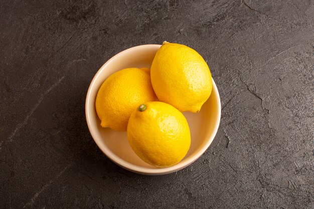Una vista superior de limones frescos amargos maduros dentro de un plato blanco entero cítricos suaves vitaminas tropicales amarillo sobre el oscuro escritorio