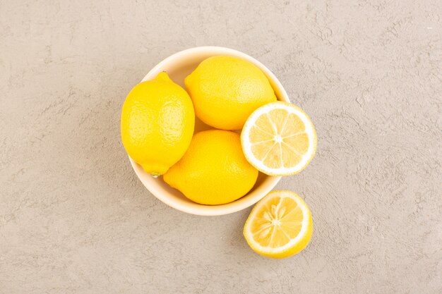 Una vista superior de limones frescos amargos maduros enteros cítricos suaves vitaminas tropicales amarillas junto con flores secas en el escritorio de crema