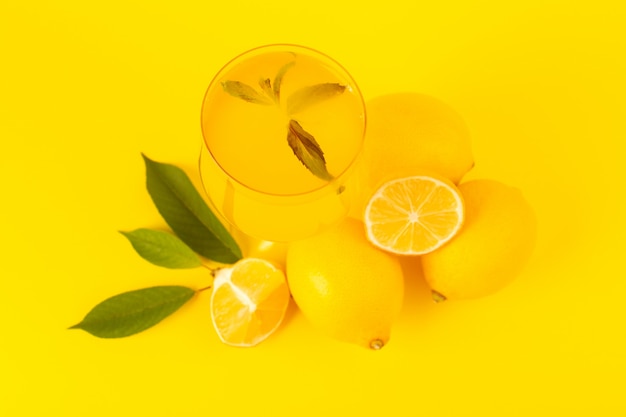 Una vista superior limones frescos amarillos frescos maduros enteros y en rodajas con bebida de limón dentro de frutas de vidrio aislado en el fondo amarillo color de cítricos