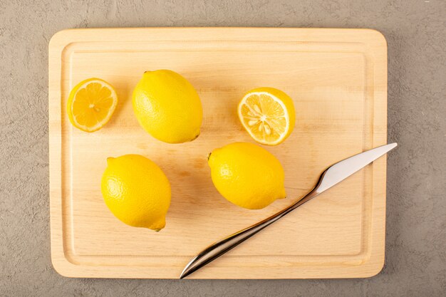 Una vista superior limones frescos amarillos maduros suaves jugosos aparecieron en el escritorio crema forrado y rebanado en el fondo gris frutas color cítrico