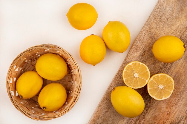 Vista superior de limones frescos en un balde con limones aislado en una tabla de cocina de madera sobre un fondo blanco.