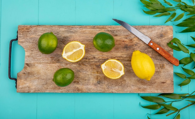 Vista superior de limones frescos y coloridos en tablero de cocina de madera con cuchillo con hojas en azul