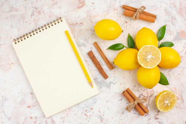 Vista superior de limones frescos cortados de limón, canela, cuaderno y lápiz amarillo sobre una superficie aislada brillante
