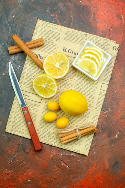 Foto gratuita vista superior de limones frescos cumcuats canela rodajas de limón en un tazón pequeño cuchillo en el periódico en la mesa de color rojo oscuro