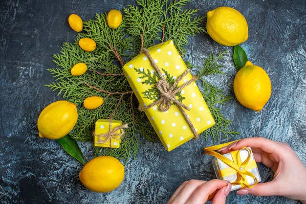 Vista superior de limones frescos con hojas kumquats en ramas de abeto mano sosteniendo una caja de regalo sobre fondo oscuro