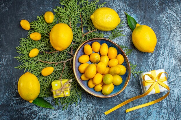 Vista superior de limones frescos con hojas de un plato con kumquats en ramas de abeto una caja de regalo sobre fondo oscuro