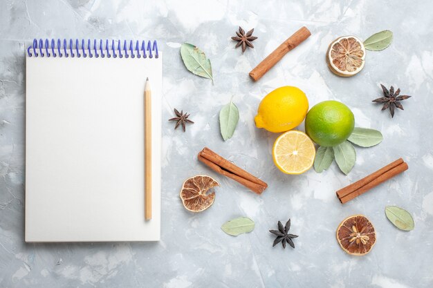 Vista superior de limones frescos jugosos y agrios con canela y bloc de notas en el escritorio blanco cítricos de frutas exóticas tropicales