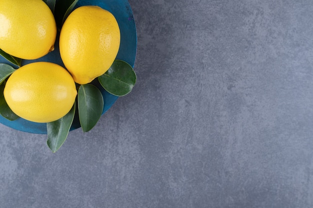 Vista superior de limones frescos en placa azul sobre fondo gris.