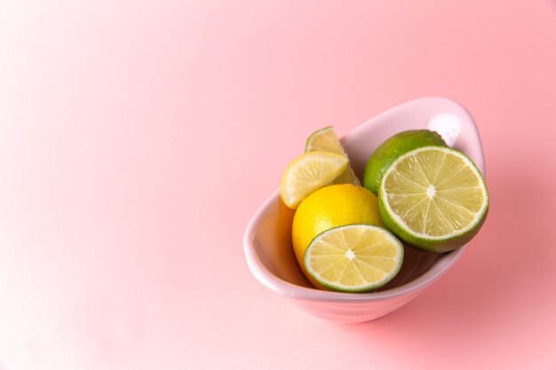 Vista superior de limones frescos con rodajas de limón dentro de la placa sobre la superficie rosa