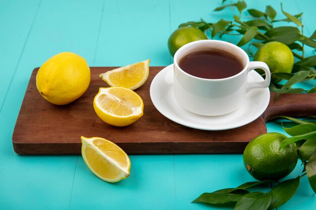 Vista superior de limones frescos en tablero de cocina de madera con una taza de té en azul