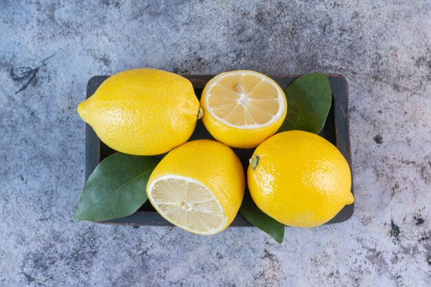 Vista superior de limones jugosos orgánicos en placa de madera sobre gris.