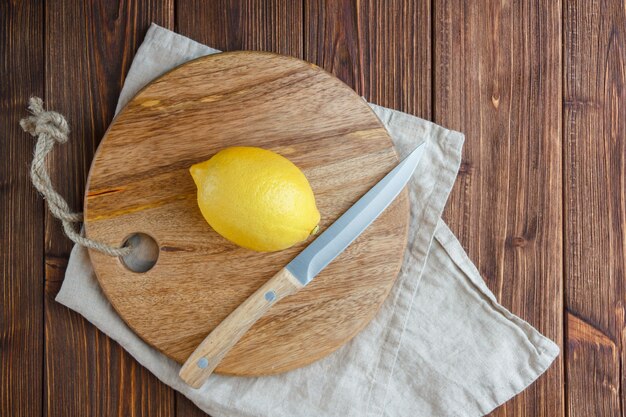 Vista superior de limones con limón sobre tabla de cortar sobre superficie de madera. vertical